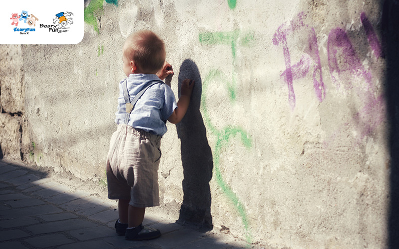 Toddler stumbling while walking by a wall.