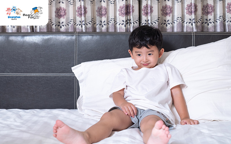Young boy sitting awkwardly on a bed.