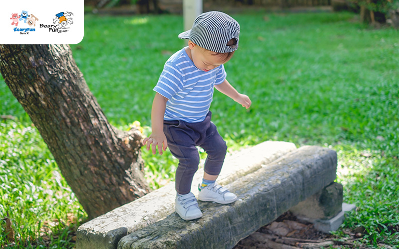 A young boy balancing on a wooden log.