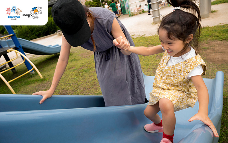 Child playing on a slide with adult supervision. 
