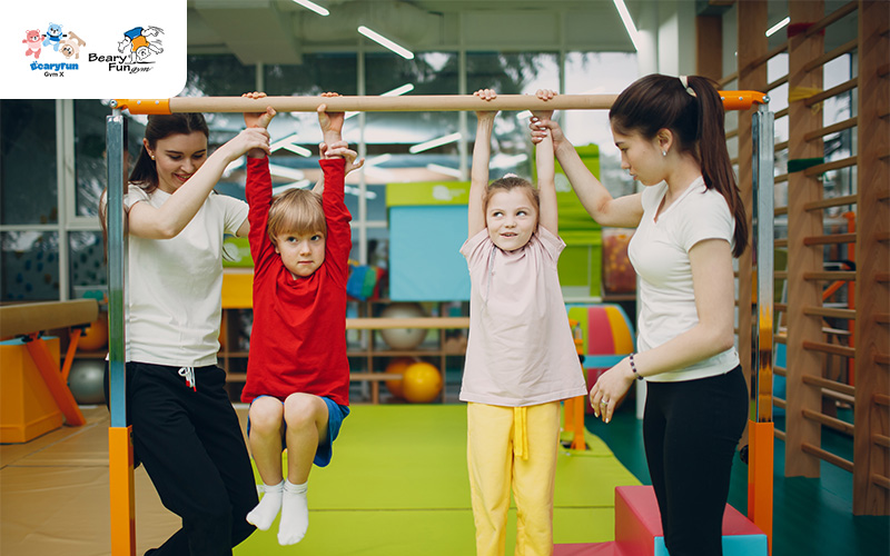 Children hanging from a bar with the help of instructors.