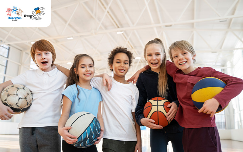 Diverse kids smiling, holding sports balls at the gym.