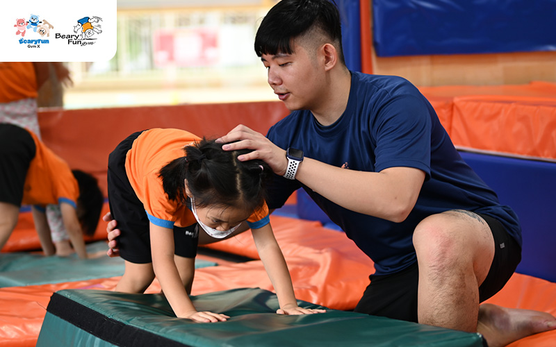 Preschooler being spotted on a gymnastics mat by coach.