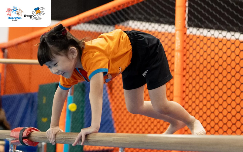 Preschooler practicing gymnastics balance on the horizontal bar.