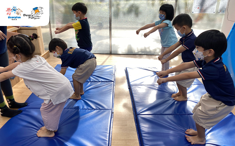 Preschoolers practicing jump and land drills on gymnastics mats.