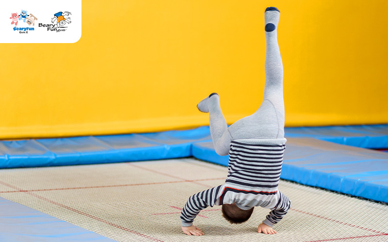 Toddler doing a handstand on a trampoline at a gym.