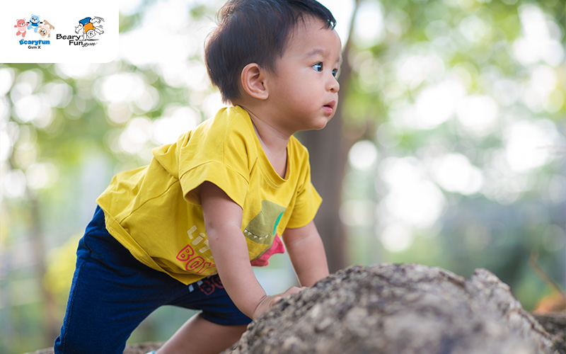 Toddler climbing a rock in a park.